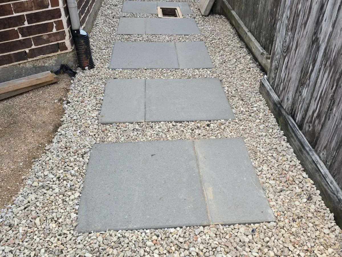 Large concrete pads in white gravel down a narrow side yard